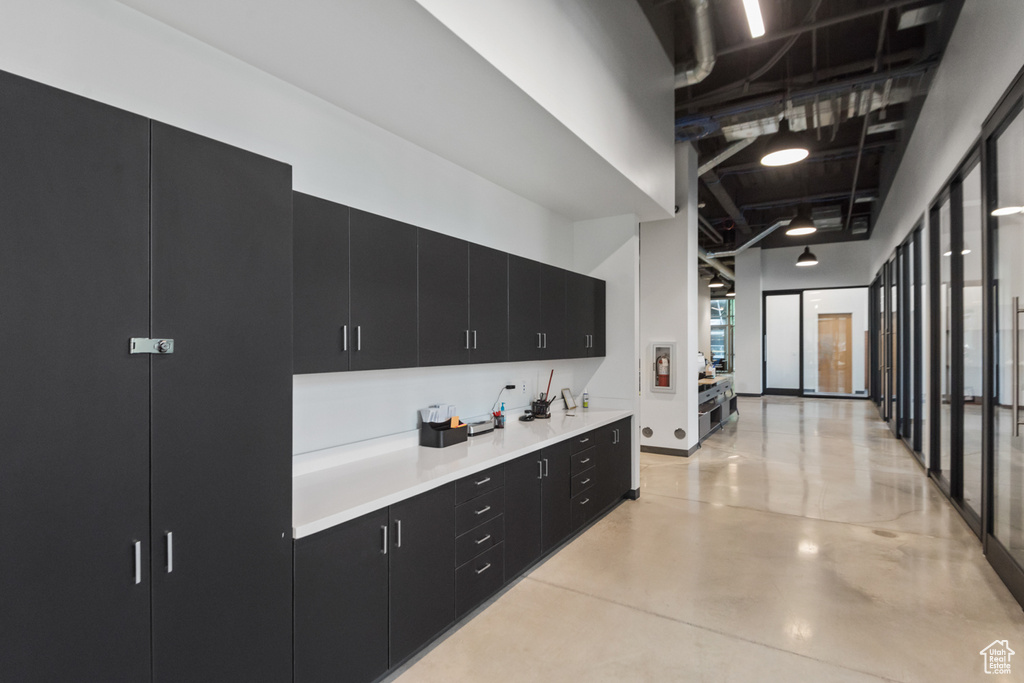 Kitchen featuring dark cabinetry, finished concrete flooring, light countertops, and a towering ceiling