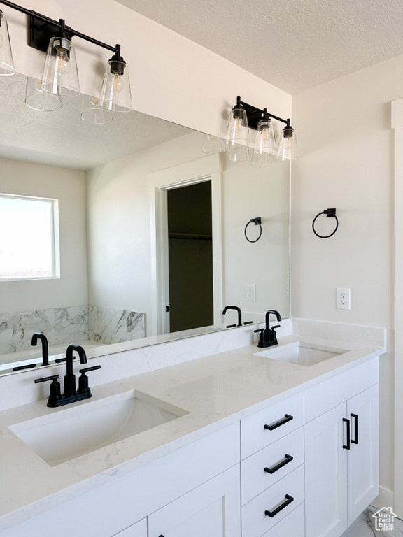 Full bathroom with double vanity, marble finish floors, and a textured ceiling