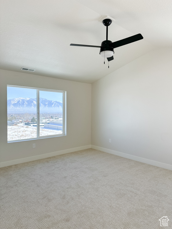 Carpeted empty room with vaulted ceiling, a ceiling fan, and baseboards