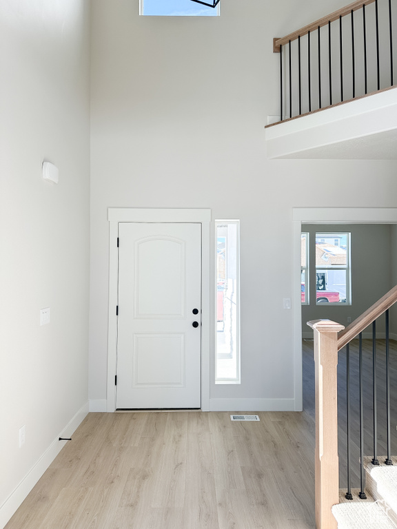 Foyer entrance featuring a towering ceiling, light wood-style flooring, baseboards, and stairs