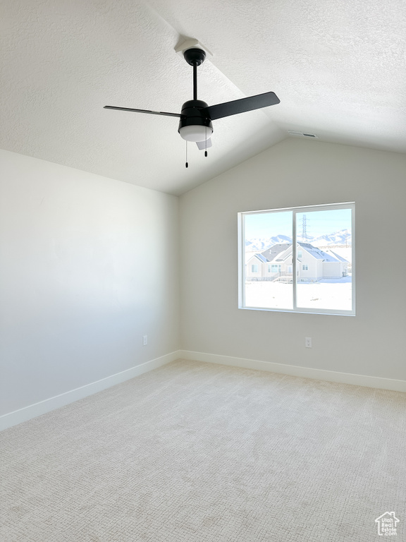 Unfurnished room featuring ceiling fan, a textured ceiling, vaulted ceiling, light colored carpet, and baseboards