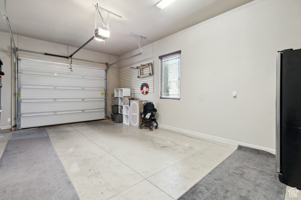 Garage with a garage door opener, refrigerator, and baseboards