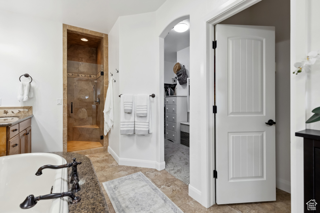 Full bathroom with a bath, vanity, a walk in closet, a stall shower, and baseboards