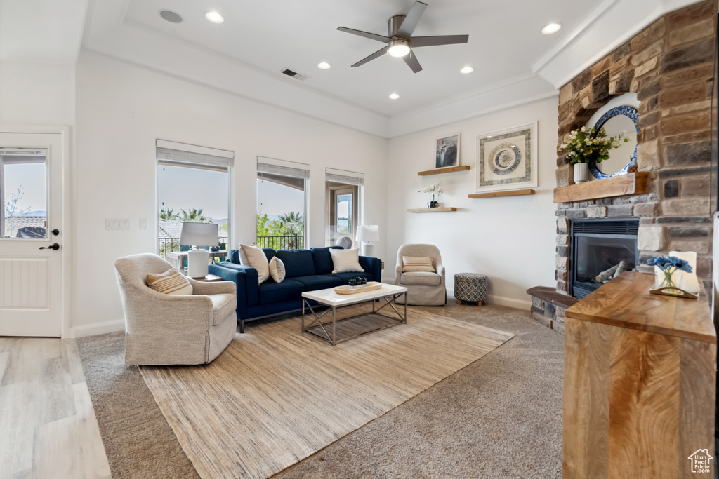 Living room featuring a stone fireplace, a ceiling fan, visible vents, and a wealth of natural light