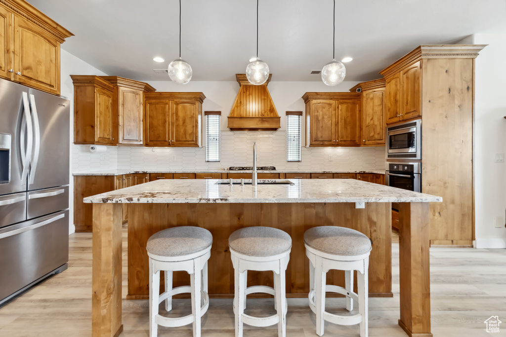Kitchen with stainless steel appliances, an island with sink, premium range hood, and backsplash