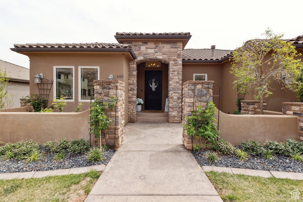 View of front of home with fence, stucco siding, stone siding, and a tile roof