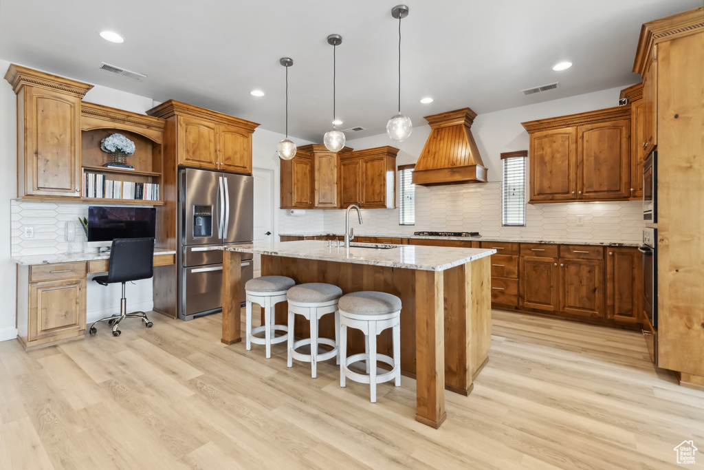 Kitchen with custom range hood, an island with sink, visible vents, stainless steel appliances, and a sink
