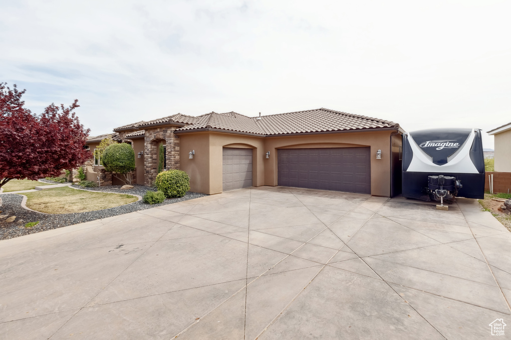 Mediterranean / spanish-style home featuring a tiled roof, stucco siding, stone siding, a garage, and driveway