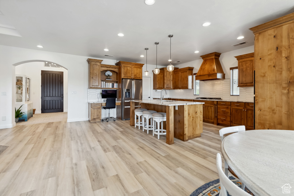 Kitchen featuring a kitchen breakfast bar, open shelves, custom exhaust hood, a sink, and stainless steel appliances