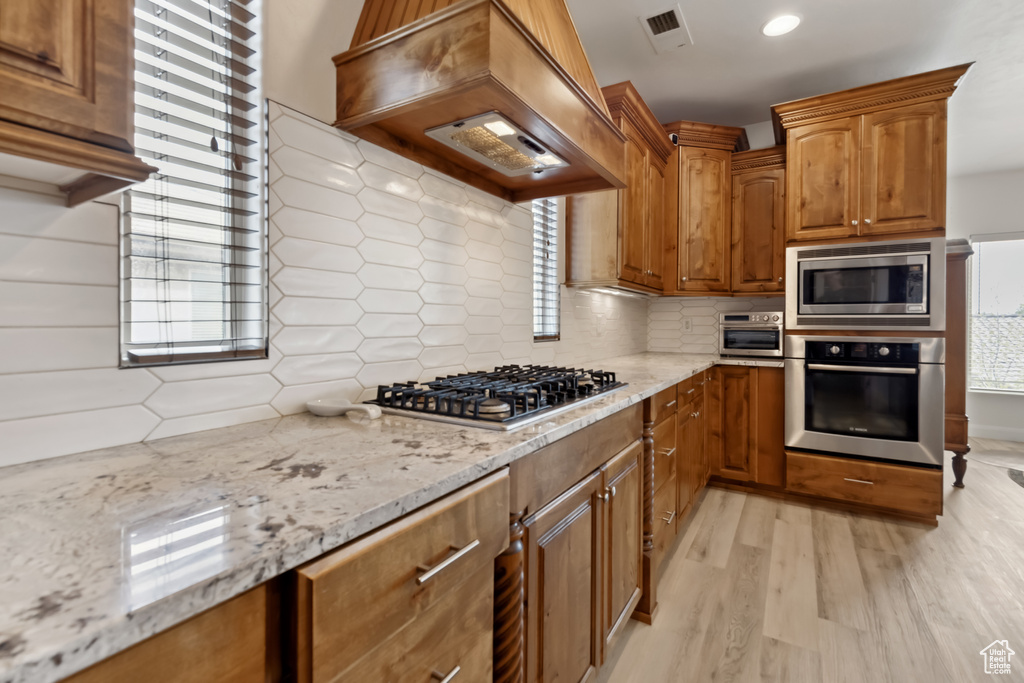 Kitchen featuring light wood-style flooring, visible vents, light stone counters, stainless steel appliances, and custom range hood