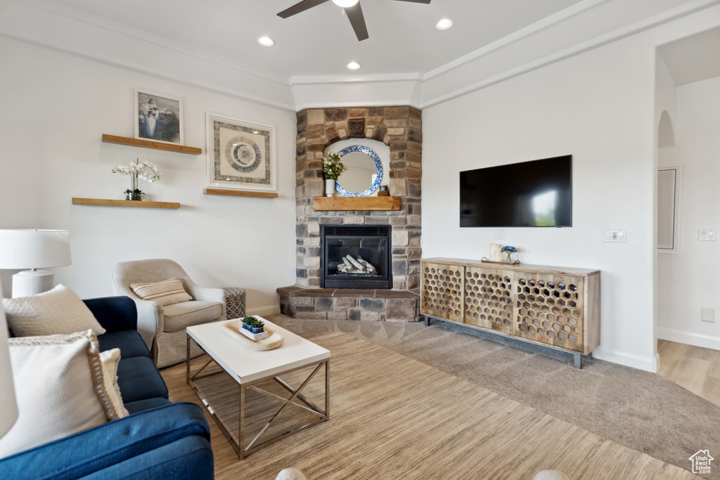 Living area featuring baseboards, a stone fireplace, crown molding, ceiling fan, and arched walkways
