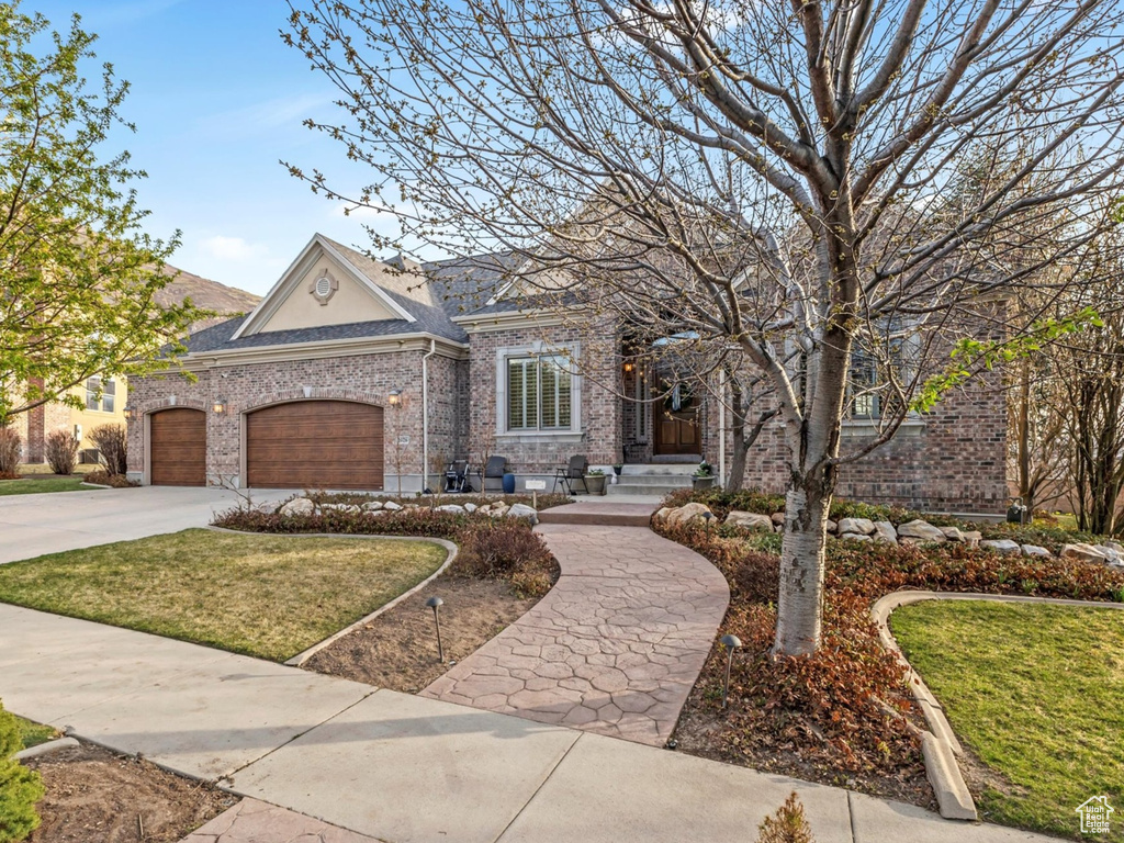 View of front facade with an attached garage, concrete driveway, a front lawn, and brick siding