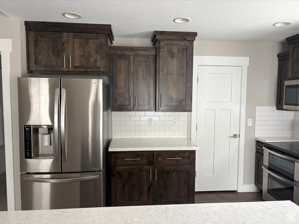 Kitchen featuring appliances with stainless steel finishes, dark brown cabinets, decorative backsplash, a textured ceiling, and recessed lighting