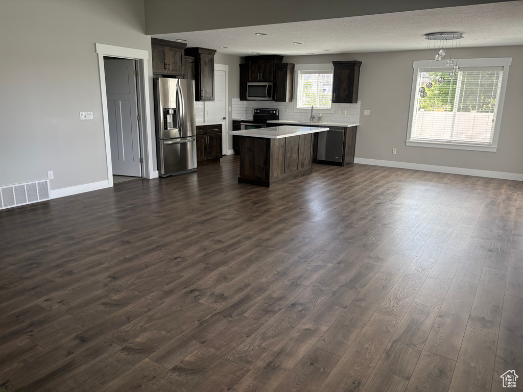 Kitchen with appliances with stainless steel finishes, open floor plan, light countertops, dark wood-style flooring, and decorative backsplash