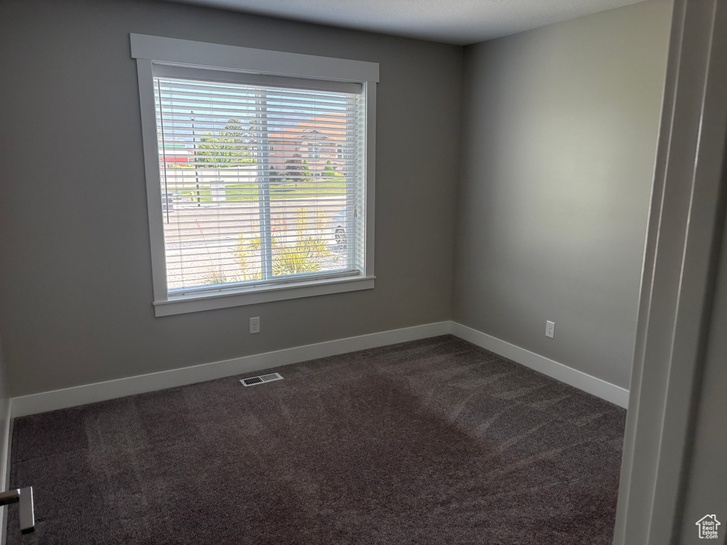 Spare room featuring dark colored carpet and baseboards