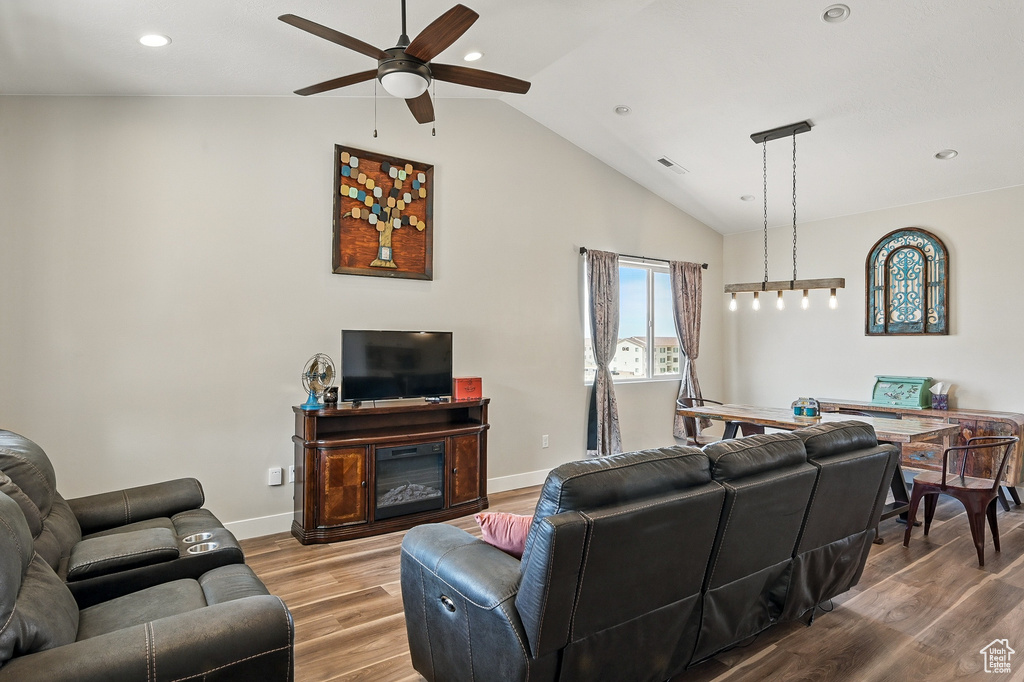 Living room featuring a ceiling fan, visible vents, vaulted ceiling, wood finished floors, and baseboards