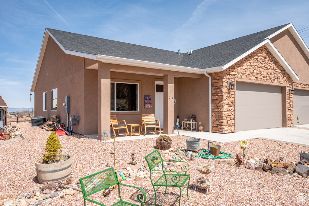 Ranch-style home featuring central AC unit, an attached garage, stone siding, stucco siding, and driveway
