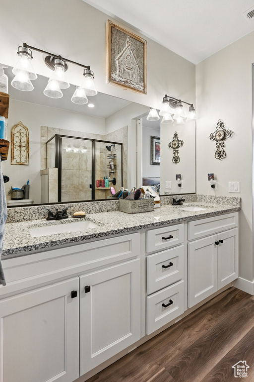 Full bathroom with double vanity, a stall shower, visible vents, a sink, and wood finished floors