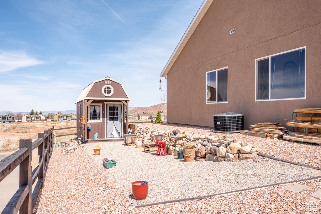View of property exterior with central air condition unit, a storage shed, fence, an outdoor structure, and stucco siding