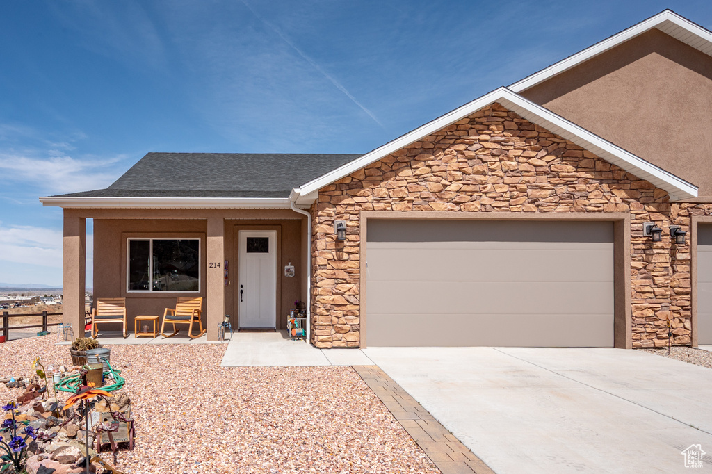 Ranch-style house with driveway, stone siding, an attached garage, a shingled roof, and covered porch