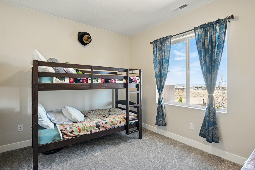 Carpeted bedroom featuring baseboards, multiple windows, and visible vents
