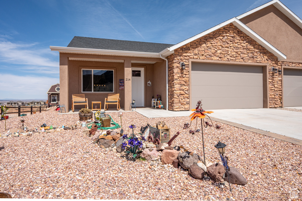 Ranch-style house with driveway, a garage, stone siding, and stucco siding