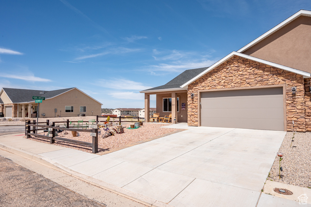 View of front of home featuring concrete driveway, stone siding, a garage, fence, and a shingled roof