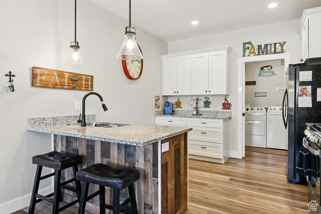 Kitchen featuring a sink, light wood-style floors, white cabinetry, washing machine and dryer, and a breakfast bar area