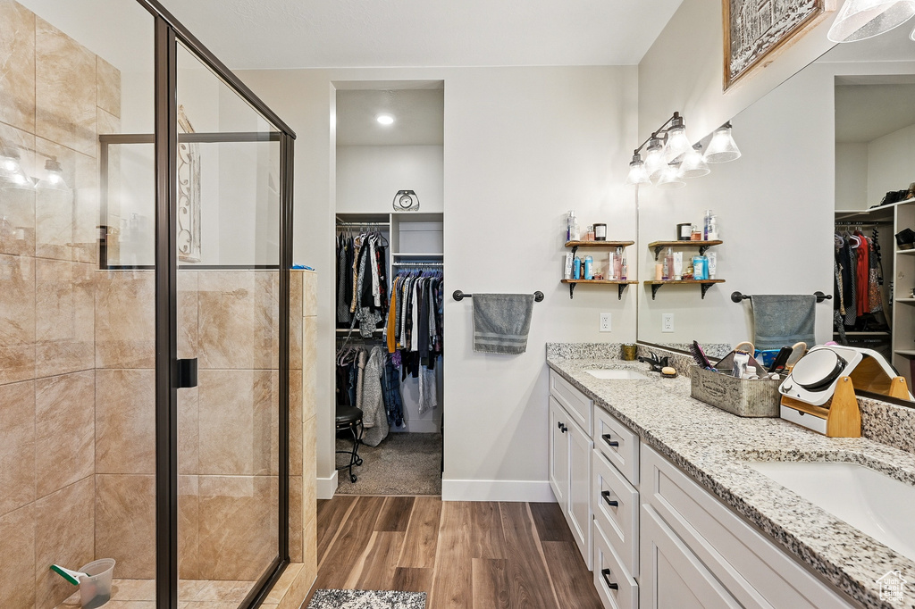 Full bathroom featuring a sink, a shower stall, double vanity, and wood finished floors