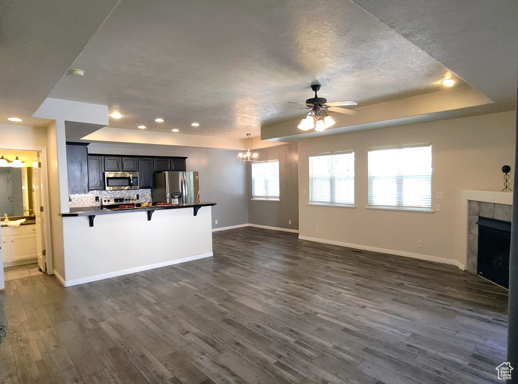 Unfurnished living room with a ceiling fan, dark wood-style flooring, a tiled fireplace, baseboards, and recessed lighting