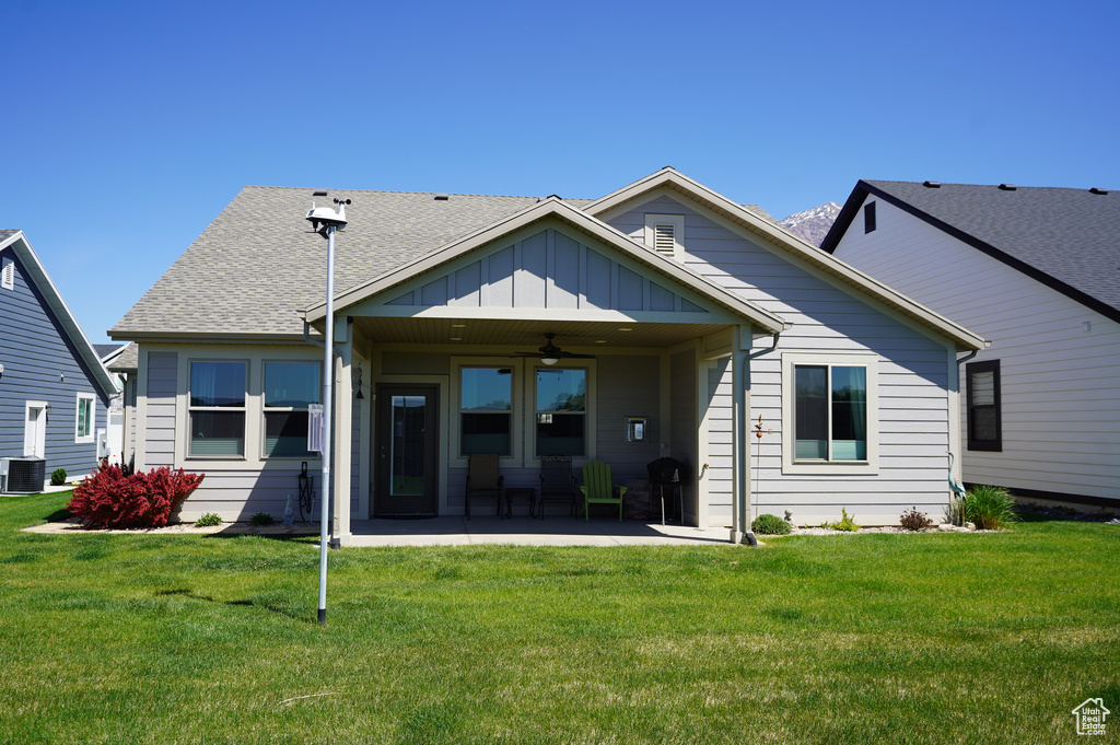 Rear view of property with board and batten siding, ceiling fan, a patio area, and a yard