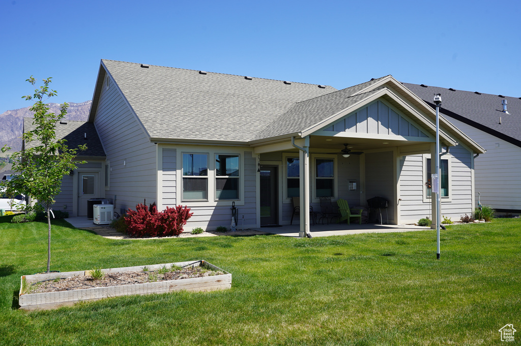 Rear view of property featuring a ceiling fan, a patio area, a yard, and a shingled roof