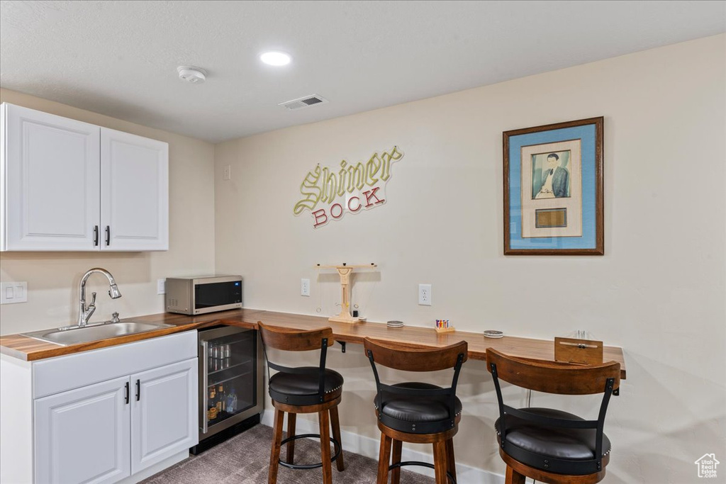Kitchen featuring white cabinets, a sink, visible vents, beverage cooler, and a breakfast bar area