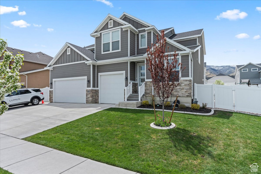 Craftsman house with a gate, stone siding, fence, board and batten siding, and a front yard