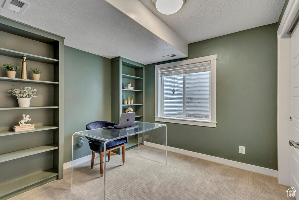 Office space featuring visible vents, built in shelves, baseboards, a textured ceiling, and carpet floors