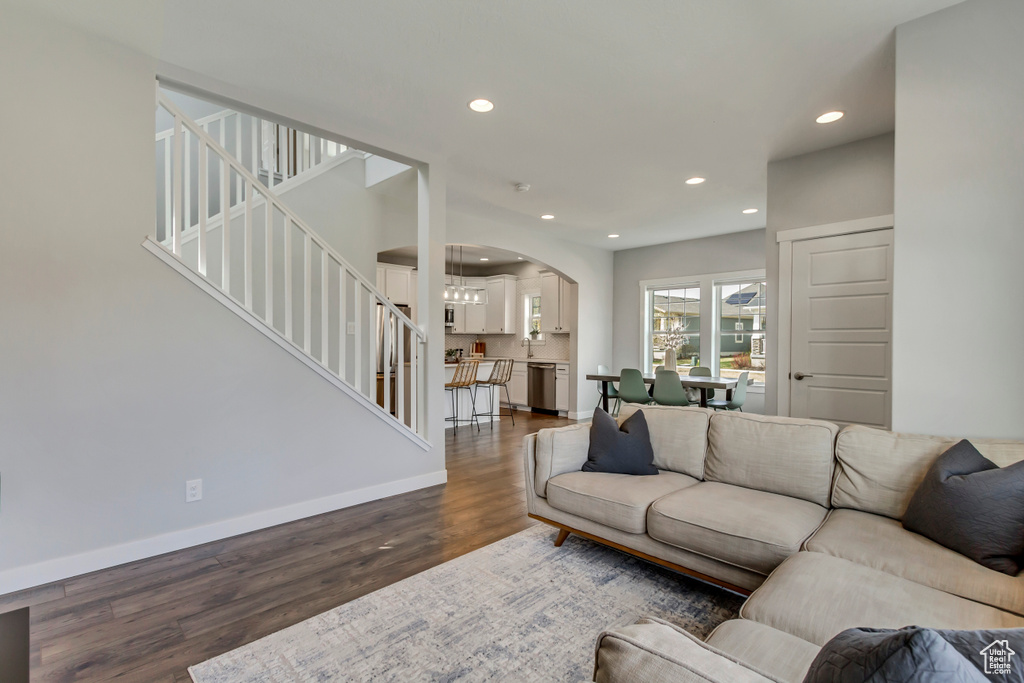 Living room with arched walkways, recessed lighting, stairway, dark wood-style flooring, and baseboards