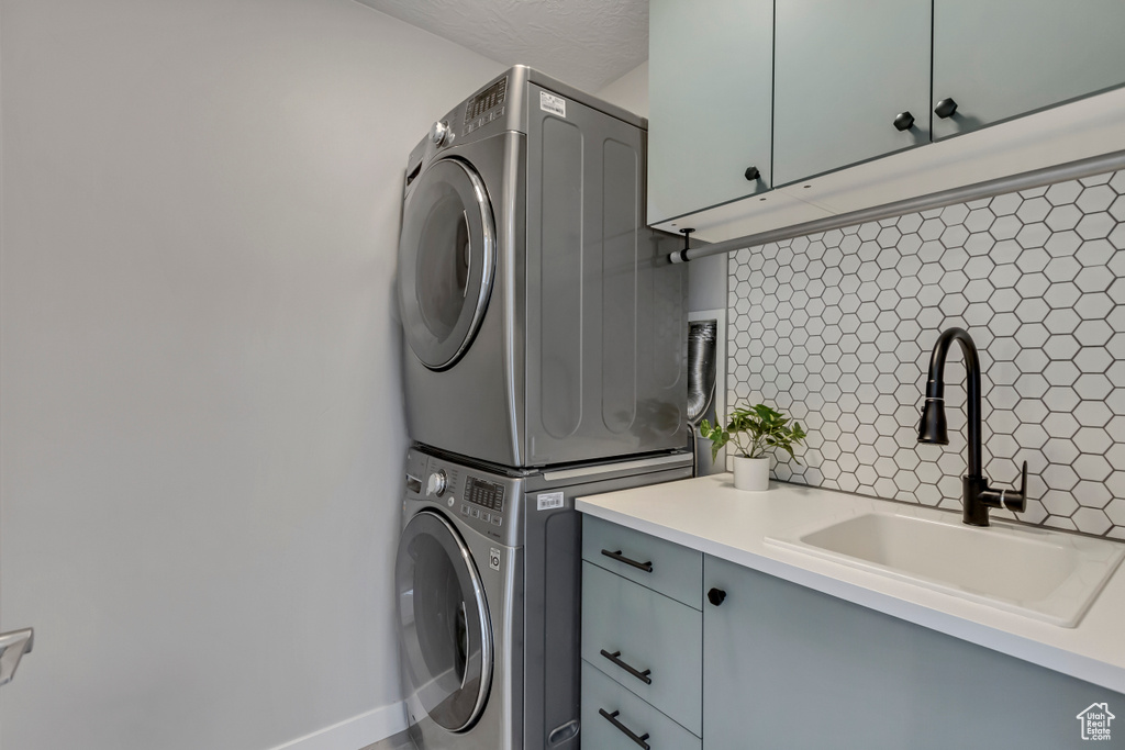 Laundry room with a sink, stacked washer and clothes dryer, and cabinet space