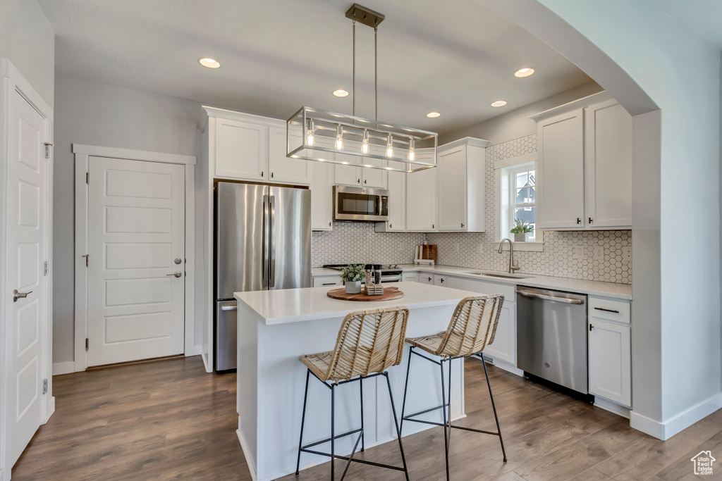 Kitchen with dark wood-type flooring, arched walkways, white cabinets, a sink, and stainless steel appliances