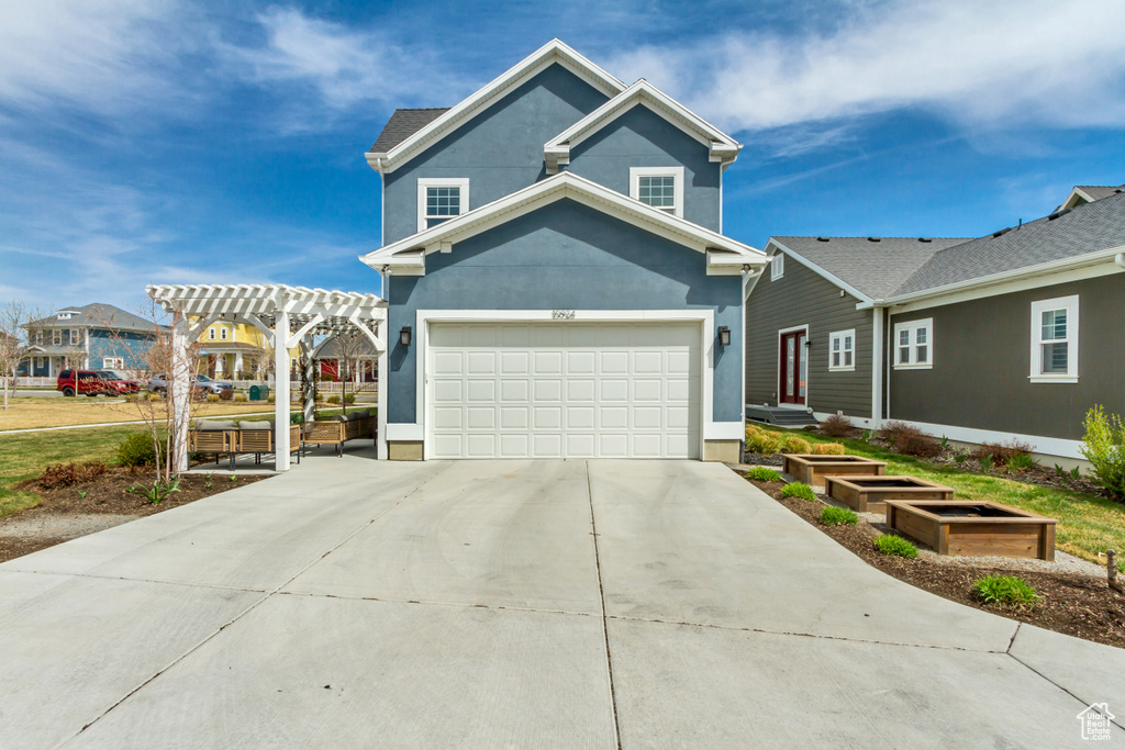 Traditional-style home with stucco siding, a garage, driveway, and a pergola