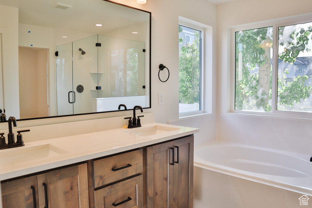 Full bathroom with healthy amount of natural light, a garden tub, a shower stall, and double vanity