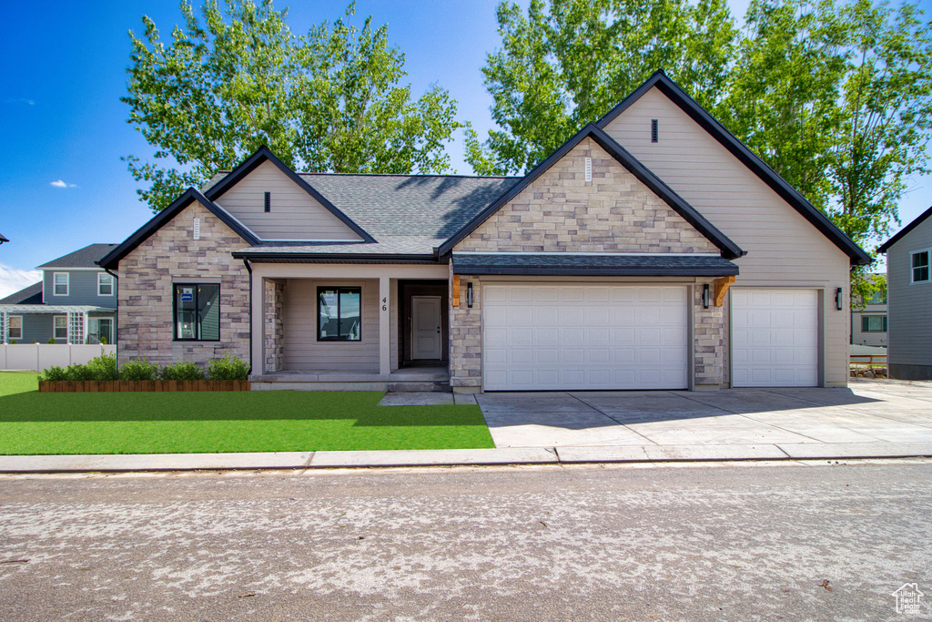 View of front of home with stone siding, driveway, a garage, and roof with shingles