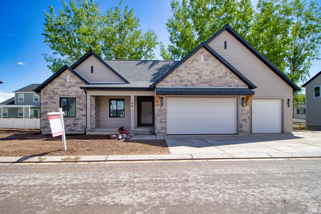 View of front of house featuring roof with shingles, an attached garage, stone siding, and driveway