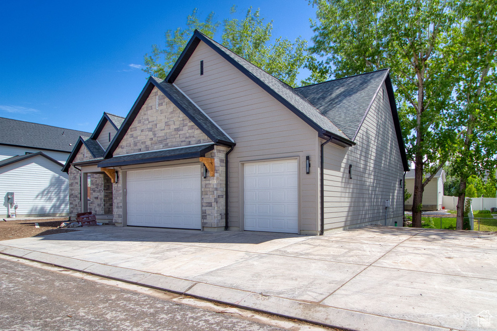 Traditional-style house with an attached garage, stone siding, fence, concrete driveway, and roof with shingles