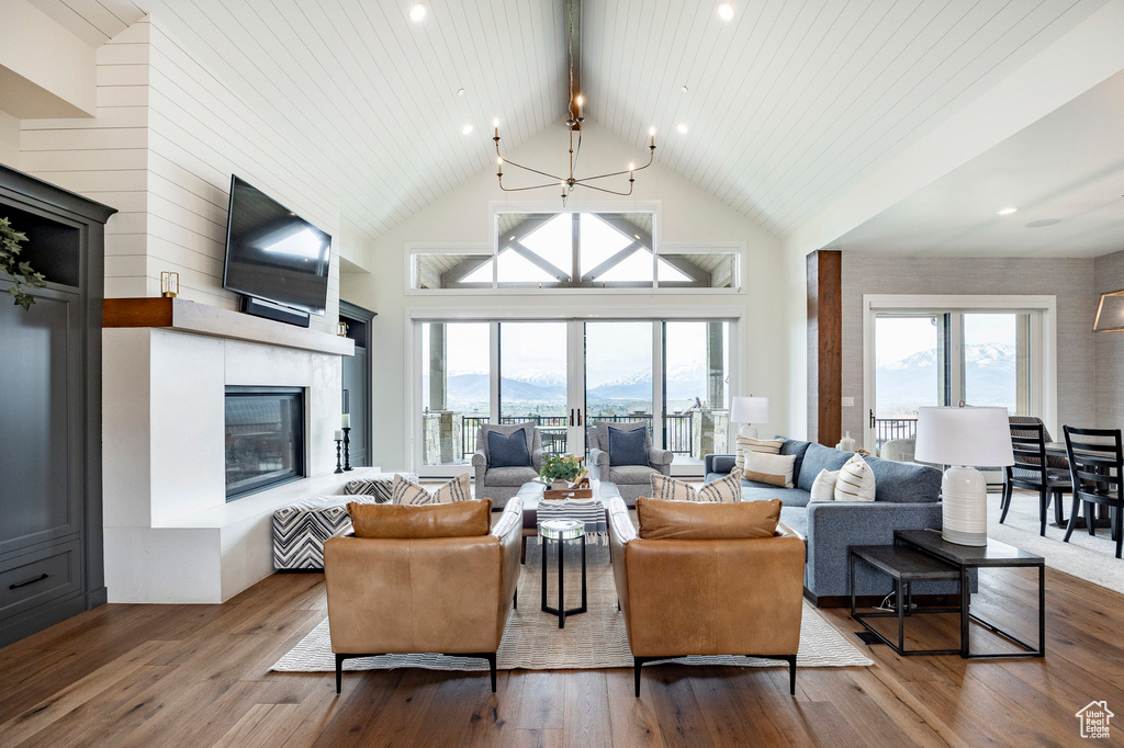 Living area with healthy amount of natural light, a glass covered fireplace, wood finished floors, beam ceiling, and high vaulted ceiling