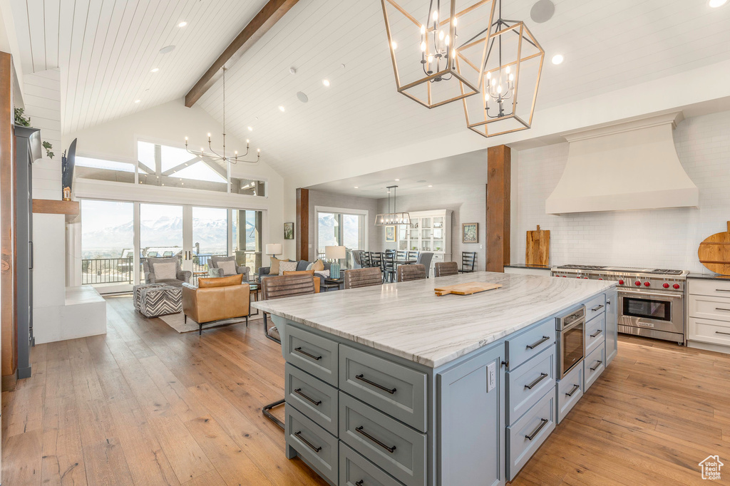 Kitchen featuring open floor plan, range with two ovens, premium range hood, a chandelier, and gray cabinetry