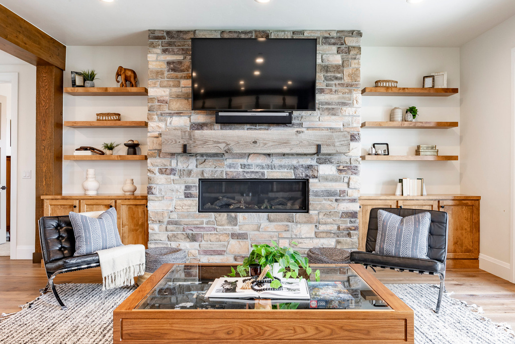 Living room featuring wood finished floors, a stone fireplace, baseboards, and recessed lighting