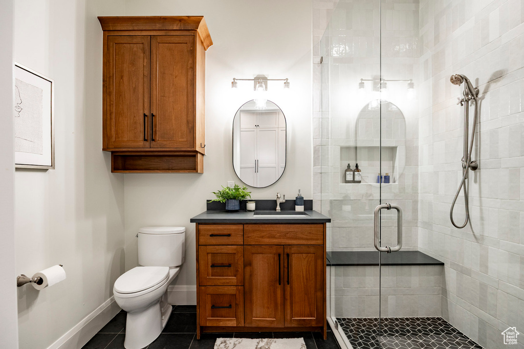 Bathroom featuring toilet, vanity, a stall shower, tile patterned flooring, and baseboards