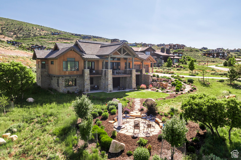 Back of house with a patio area, an outdoor fire pit, stone siding, a standing seam roof, and a lawn