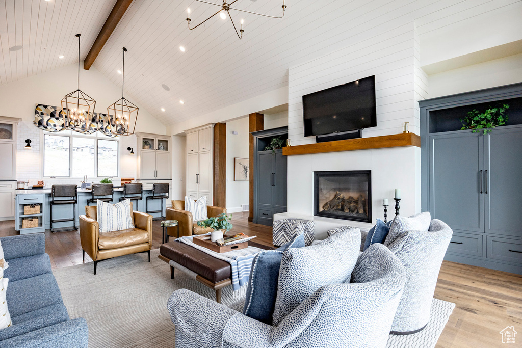 Living room featuring a chandelier, light wood-style floors, a fireplace, beamed ceiling, and high vaulted ceiling