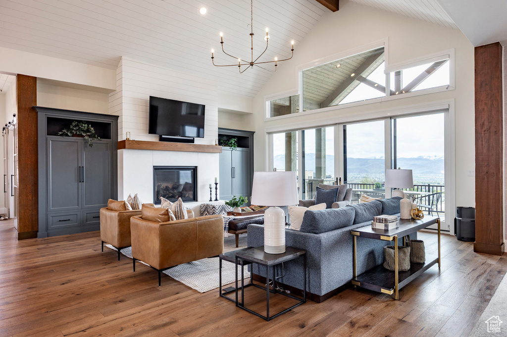 Living room with wood-type flooring, high vaulted ceiling, plenty of natural light, a chandelier, and beam ceiling